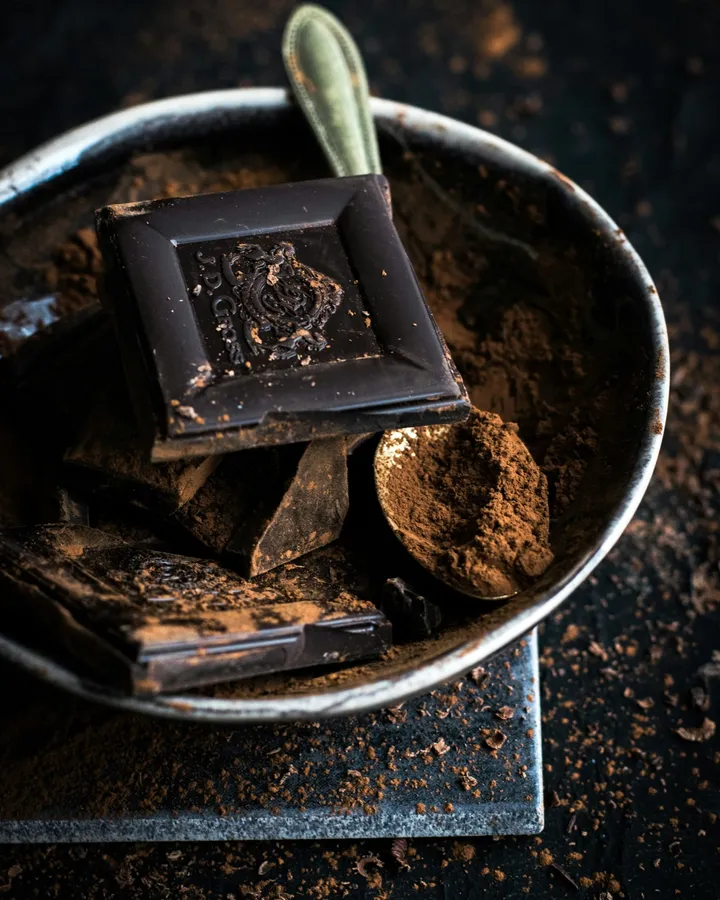 Squares of dark chocolate and a scoop of cocoa in a metal bowl.
