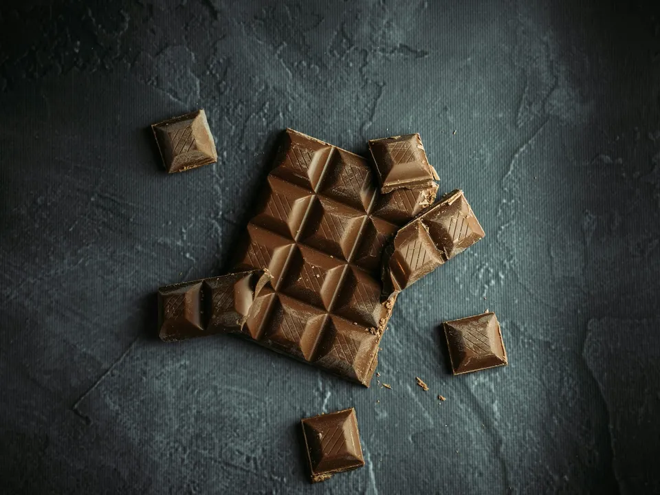 A chocolate bar broken into pieces on a slate surface.